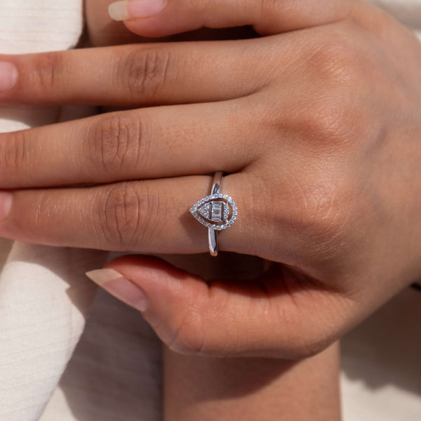 An elegant hand is adorned with Minifora's Eclipse Harmony Diamond Ring. This ring features a central lab-created emerald-cut diamond, surrounded by a halo of pavé-set diamonds that continue down the slender 14K white gold band.