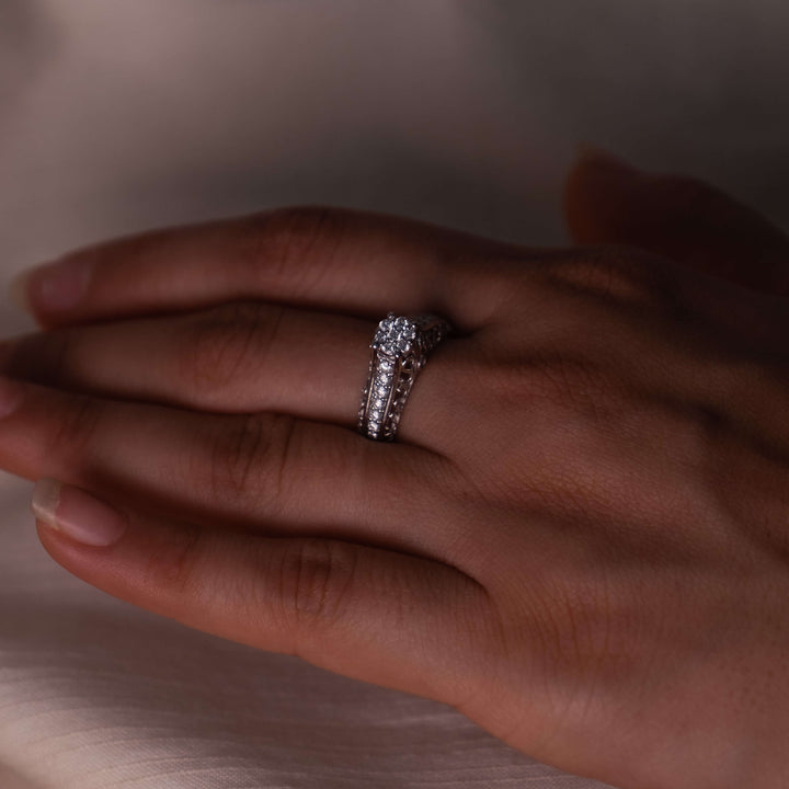 A hand elegantly presents the Eternal Filigree Radiance Ring by Minifora, set against a soft, translucent backdrop. This exquisite ring features a lavish display of lab-created diamonds set in a 14K white gold band with filigree detailing. The central cluster of diamonds creates a dazzling focal point, while the band's pavé diamonds extend the brilliance around the finger.