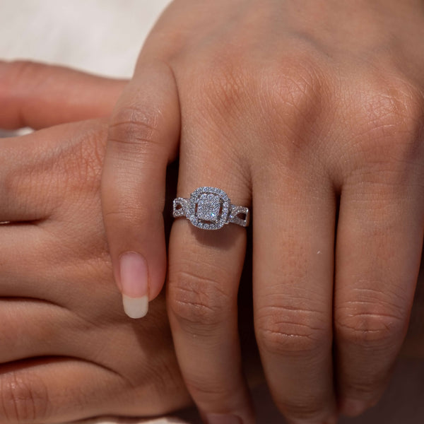 A hand models Minifora's Eternal Radiance Cluster Ring. This stunning 14K white gold ring boasts a square cluster of lab-grown diamonds at its heart, surrounded by a halo of smaller diamonds, with additional diamonds adorning the band's shoulders in an elegant display of Minifora's commitment to sustainable luxury.