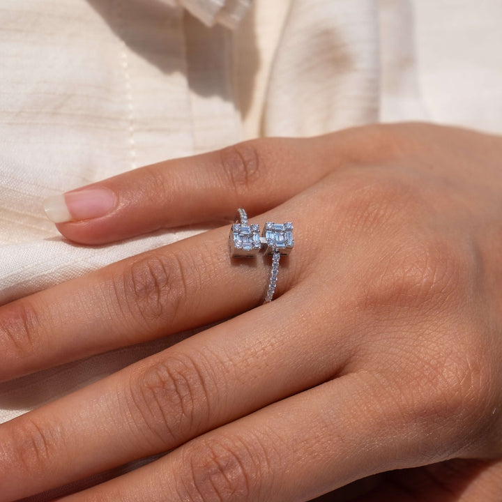 A close-up view of a hand gracefully displaying two elegant engagement rings from Minifora. Both rings feature prominent, square-cut lab-grown diamonds set in 14k white gold bands, one with a simple solitaire setting and the other encircled by smaller diamonds for a touch of added sparkle. 