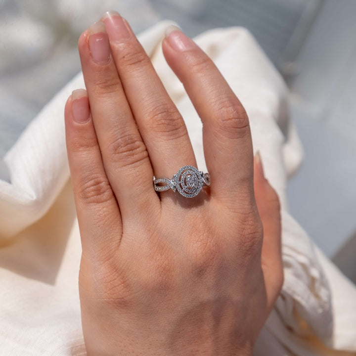 An elegant hand presents a Minifora Halo Grandeur engagement ring, showcasing a central lab-grown diamond encircled by a halo of smaller diamonds. The intricate band, crafted from 14k white gold, features a detailed pave setting that enhances the ring's brilliance.