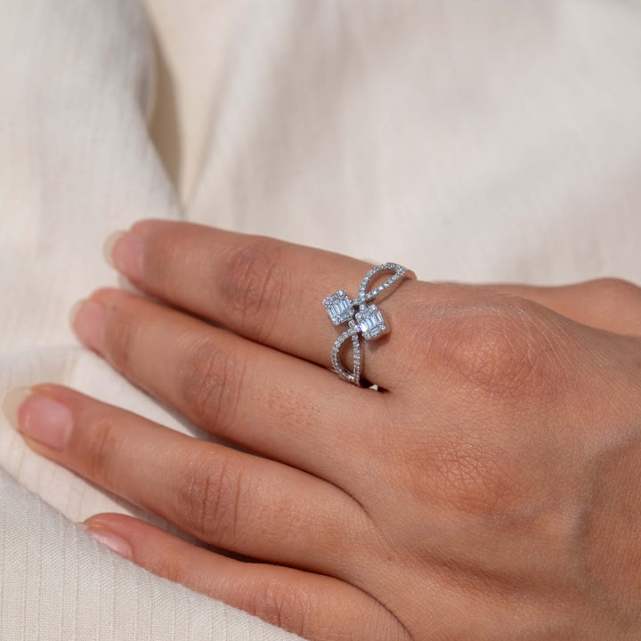 Resting against an ivory linen backdrop, a hand gracefully models a captivating Minifora 'Interstellar' engagement ring. This unique piece features two square-cut lab-grown diamonds, securely set on a cross-band design of 14k white gold, which is intricately adorned with a multitude of smaller diamonds, lending a celestial sparkle to the overall design.