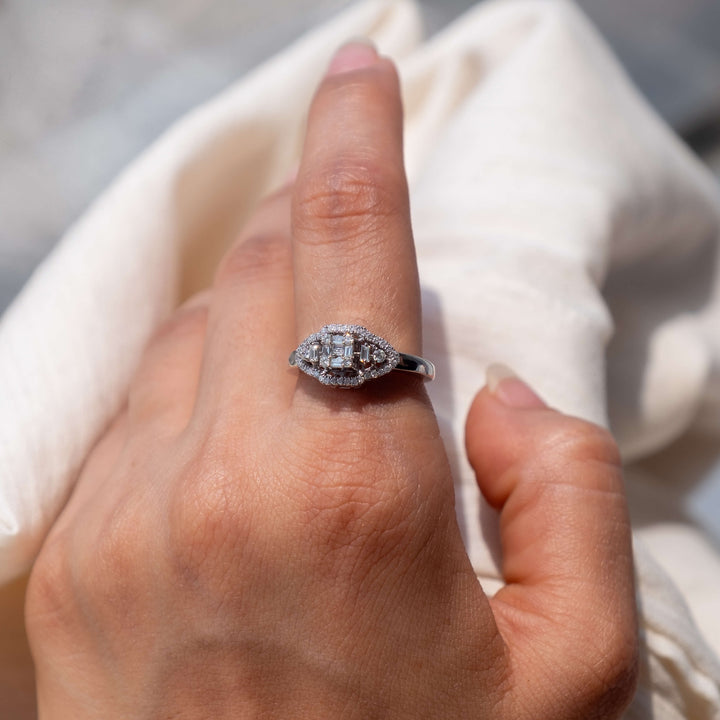 Showcasing Minifora's 'Luminous Elegance' ring worn on a hand over an off-white linen backdrop. The ring features a symmetrical, geometric design with a central lab-grown diamond highlighted by a halo and side stones. Set in polished 14k white gold, the band is partially visible and encrusted with diamonds.