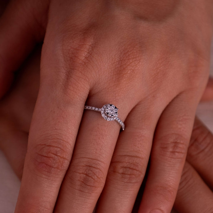 A close-up image showcasing a Minifora brand ring on a person's finger. The ring features a central lab-grown diamond, set in a radiant halo design, encircled by smaller diamonds on a delicate 14k white gold band.